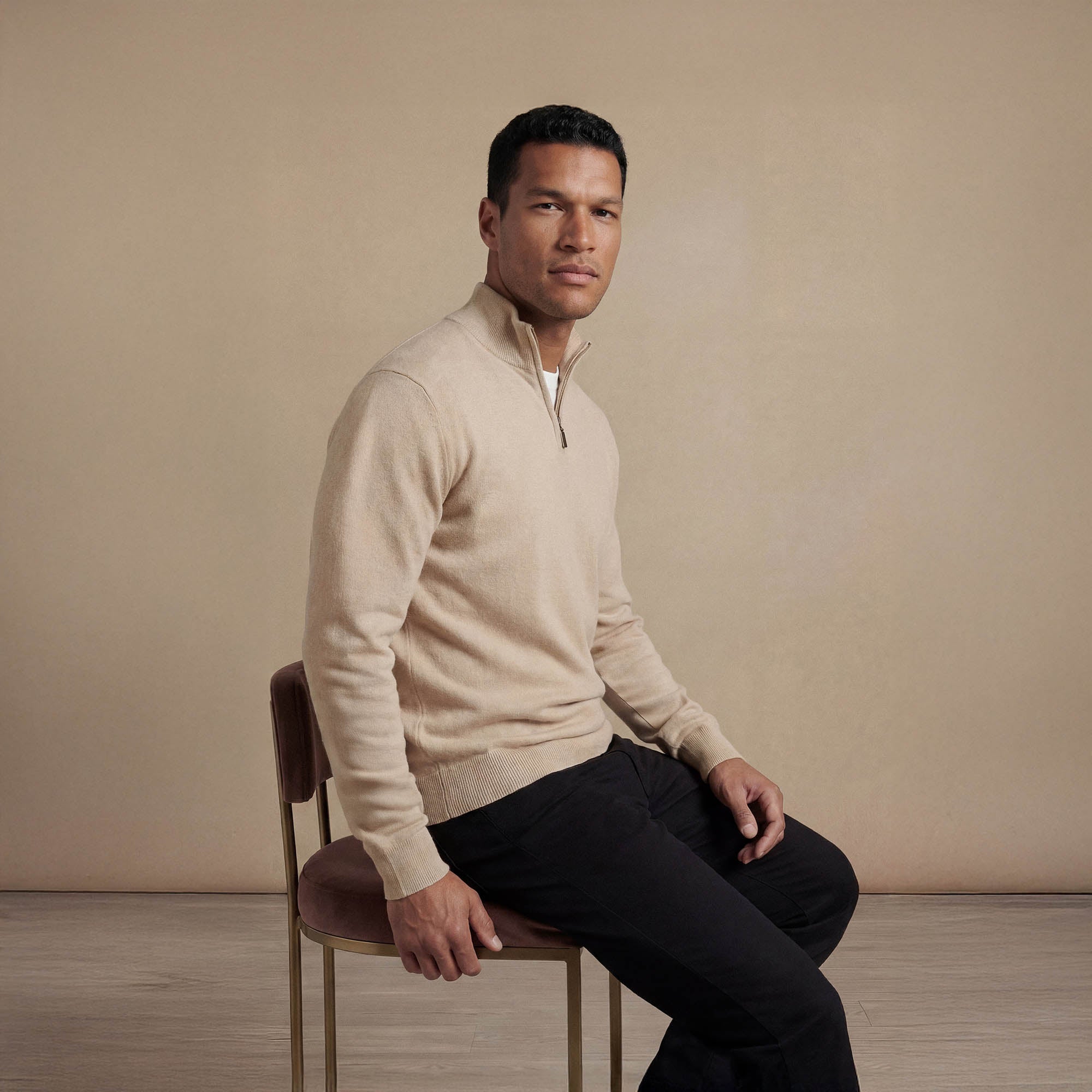 Man wearing a navy half zip jumper, seated view. |beige pearl