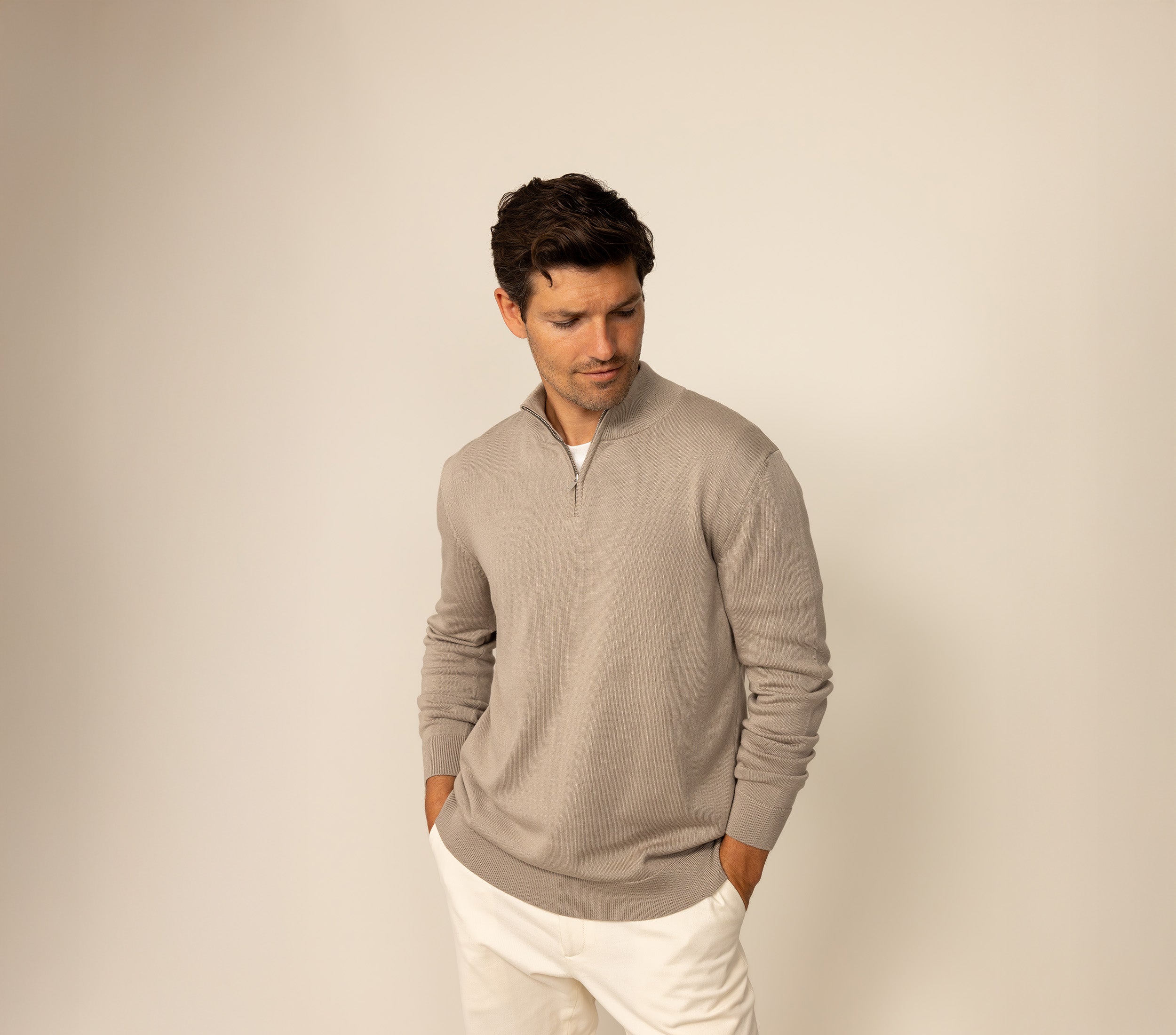 Man wearing a beige jumper and white chinos against a plain background