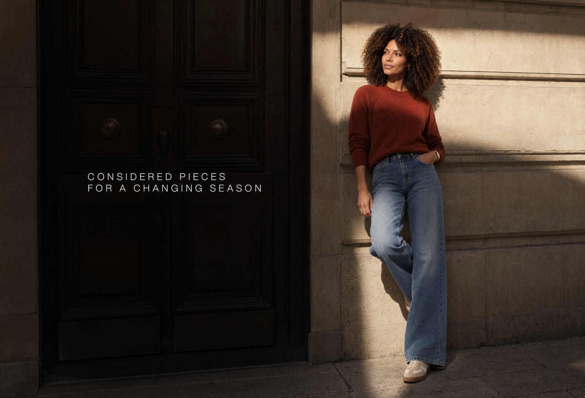 Rust-coloured MARAME knitwear with denim by a stone doorway