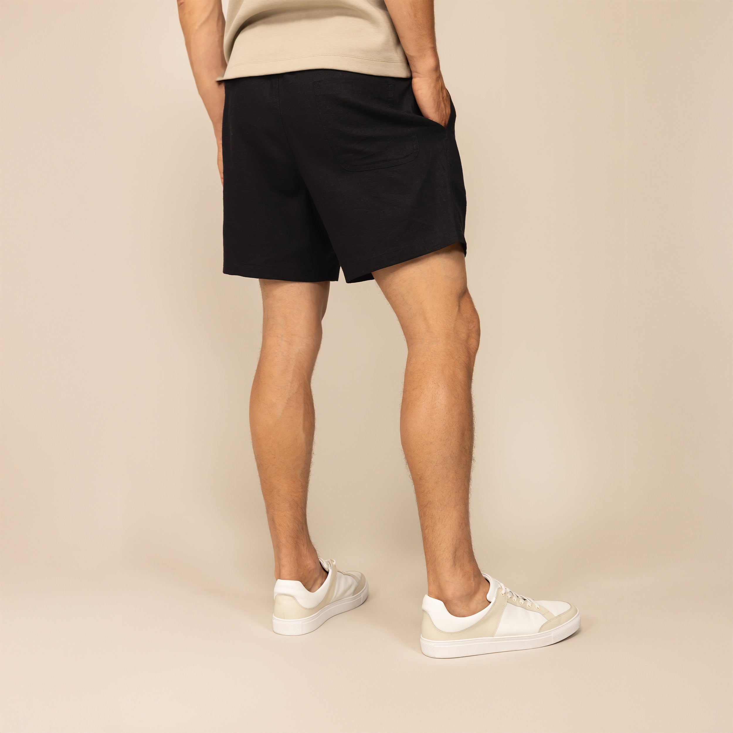 Man wearing black casual linen blend shorts, rear view.