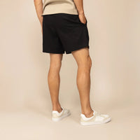 Man wearing black casual linen blend shorts, rear view. |black