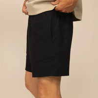 Man wearing black casual linen blend shorts, side view.