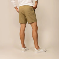 Man wearing casual linen blend shorts in natural sand, rear view. |barley green