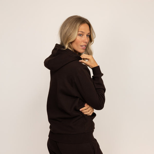 Woman wearing cotton fleece hoodie in Smoked Brown, rear view.