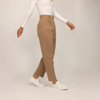 Woman wearing Marame High-Waisted Tapered Trousers in Caramel, front view.