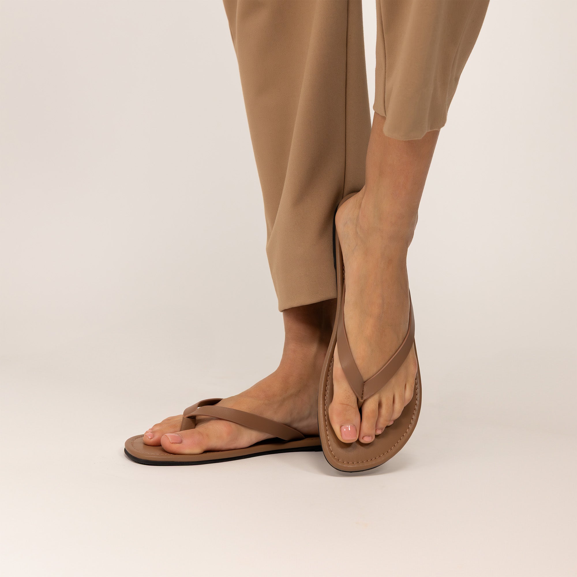Woman wearing Marame Leather Flip Flops in Brown, front view.